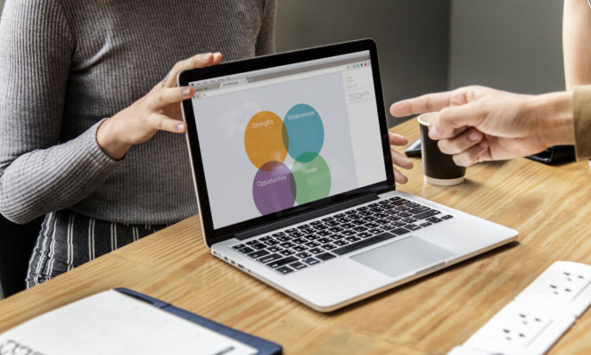Photo of laptop with people discussing what's on the screen